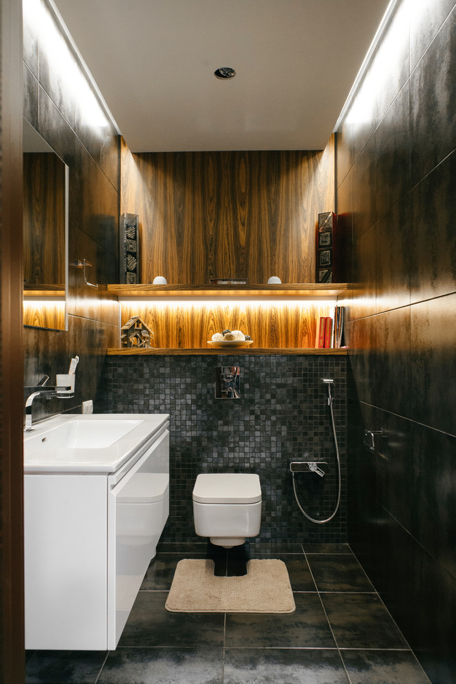 Foto på ett funkis toalett, med släta luckor, vita skåp, en vägghängd toalettstol, svart kakel, ett integrerad handfat och grått golv