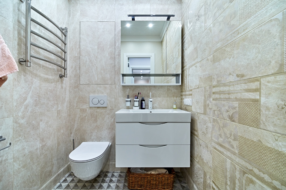 Inspiration för ett funkis vit vitt toalett, med släta luckor, vita skåp, en vägghängd toalettstol, beige kakel, ett integrerad handfat och flerfärgat golv