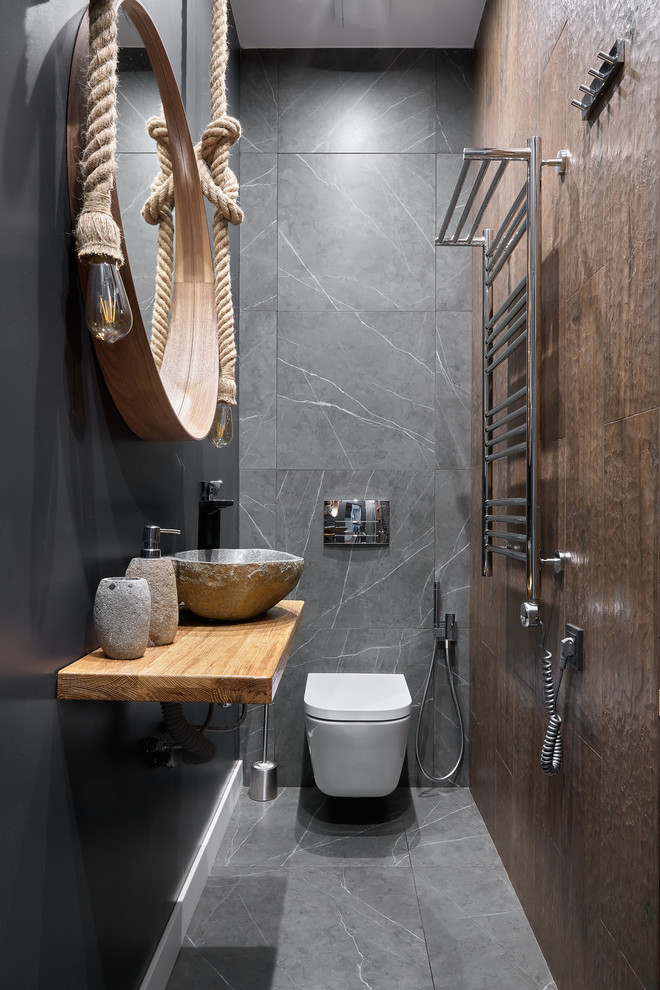 Пример оригинального дизайна: туалет в современном стиле с инсталляцией, коричневой плиткой, серой плиткой, настольной раковиной, серым полом, серыми стенами, столешницей из дерева и коричневой столешницей