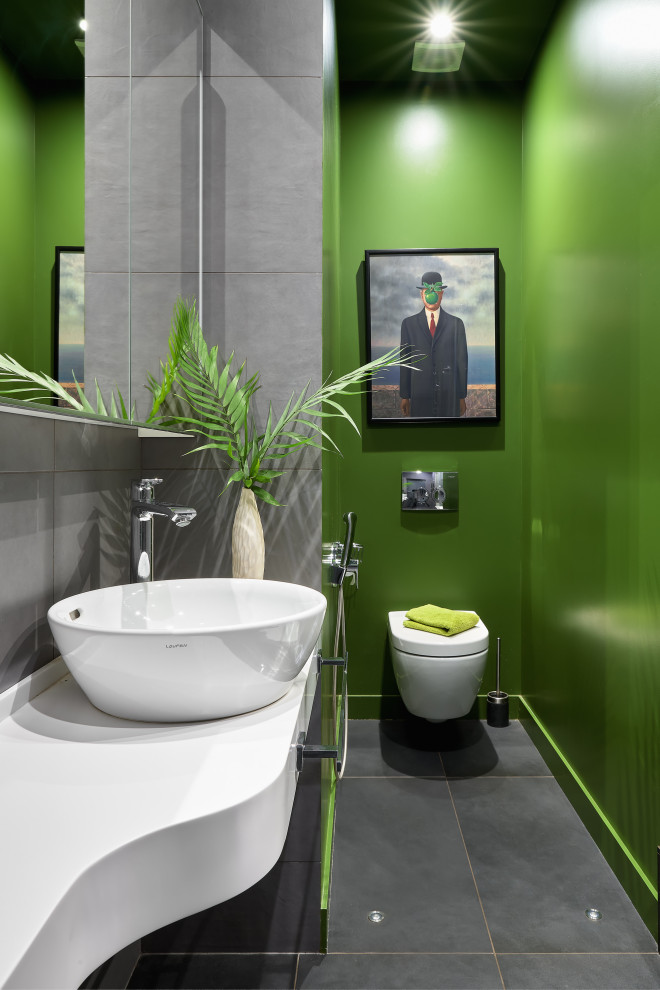 This is an example of a contemporary cloakroom in Moscow with flat-panel cabinets, black cabinets, a wall mounted toilet, grey tiles, green walls, a vessel sink, grey floors and white worktops.