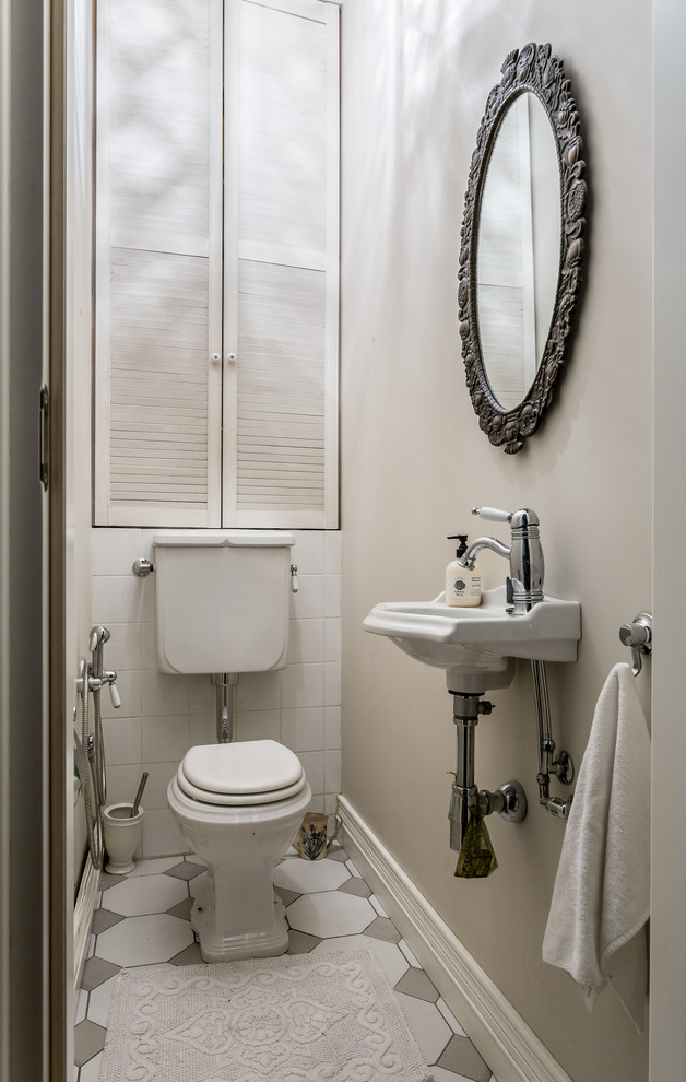 Inredning av ett klassiskt toalett, med en toalettstol med separat cisternkåpa, beige väggar och ett väggmonterat handfat