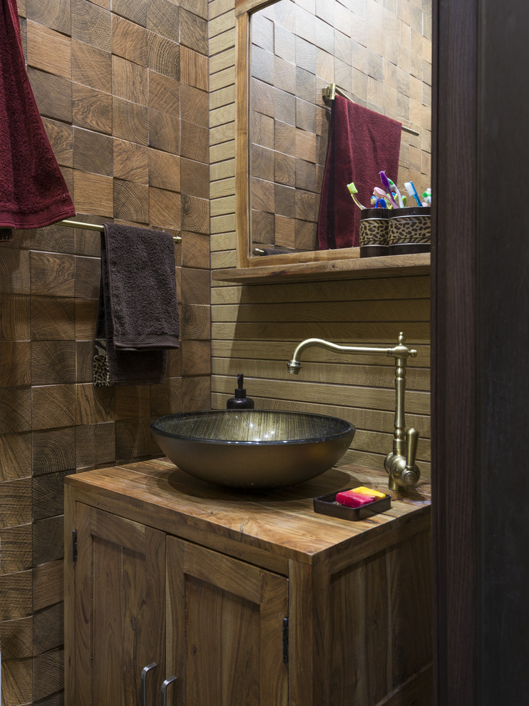 Bild på ett lantligt brun brunt toalett, med skåp i shakerstil, skåp i mellenmörkt trä, brun kakel, ett fristående handfat och träbänkskiva