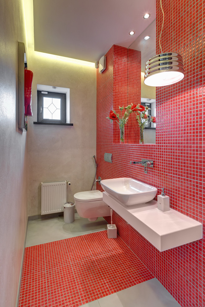 Immagine di un bagno di servizio minimal di medie dimensioni con WC sospeso, piastrelle rosse, piastrelle a mosaico, pareti multicolore, pavimento con piastrelle a mosaico, lavabo a bacinella, top in superficie solida, pavimento rosso e top bianco