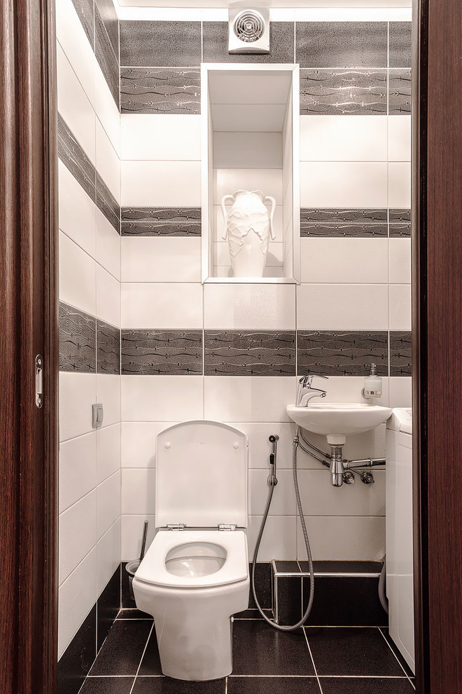 На фото: туалет среднего размера в современном стиле с раздельным унитазом, черно-белой плиткой, удлиненной плиткой, белыми стенами, полом из керамогранита, подвесной раковиной и черным полом с