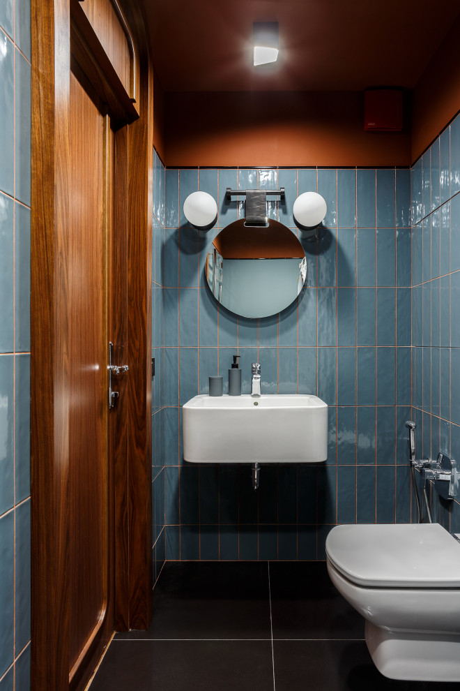 Moderne Gästetoilette mit blauen Fliesen, blauer Wandfarbe, Wandwaschbecken und schwarzem Boden in Moskau
