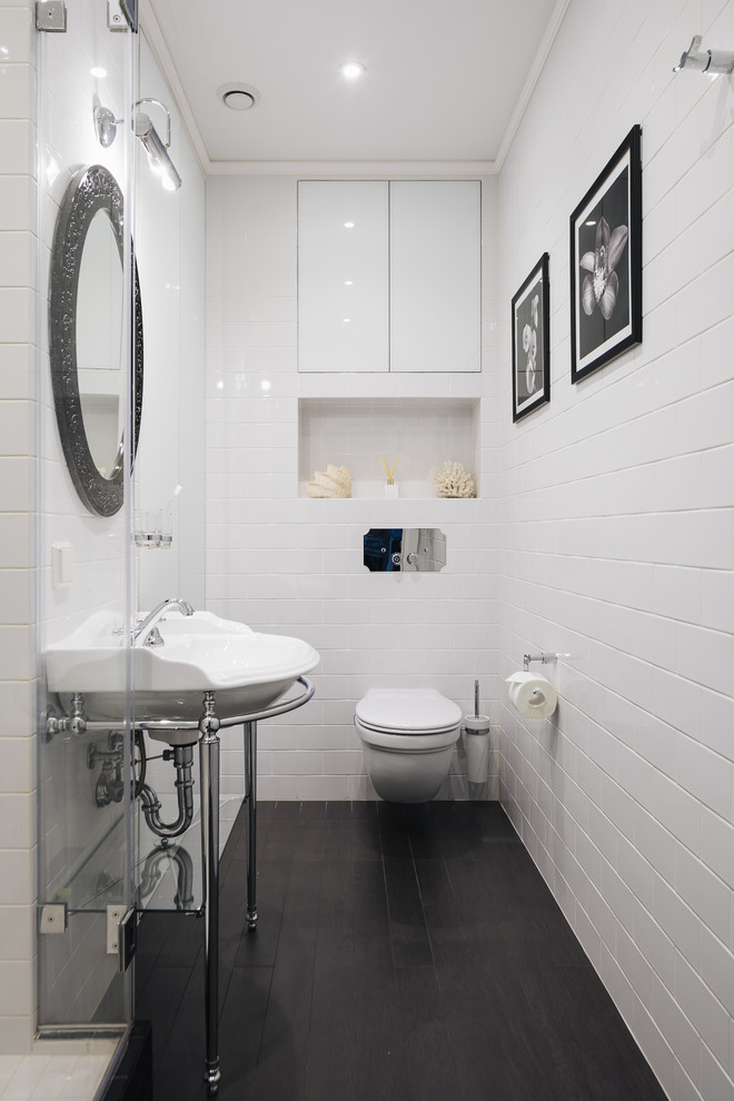 サンクトペテルブルクにあるトランジショナルスタイルのおしゃれなトイレ・洗面所 (壁掛け式トイレ、白いタイル、コンソール型シンク、黒い床、照明) の写真