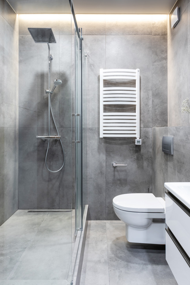 Modern inredning av ett litet badrum, med släta luckor, vita skåp, en vägghängd toalettstol, grå kakel, porslinskakel, grå väggar, klinkergolv i porslin, ett väggmonterat handfat och grått golv