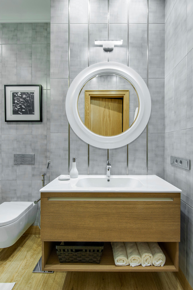 Idee per un bagno di servizio design con ante lisce, WC sospeso, piastrelle grigie, lavabo integrato, ante in legno chiaro, parquet chiaro e pavimento beige
