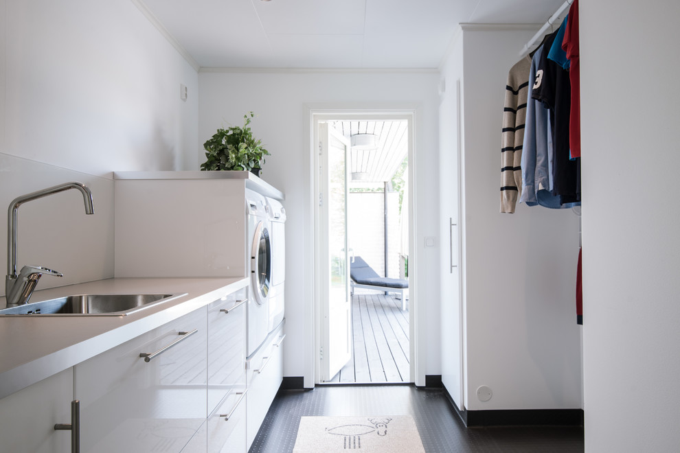 Idéer för funkis parallella vitt tvättstugor, med en nedsänkt diskho, släta luckor, vita skåp, vita väggar, en tvättmaskin och torktumlare bredvid varandra och svart golv
