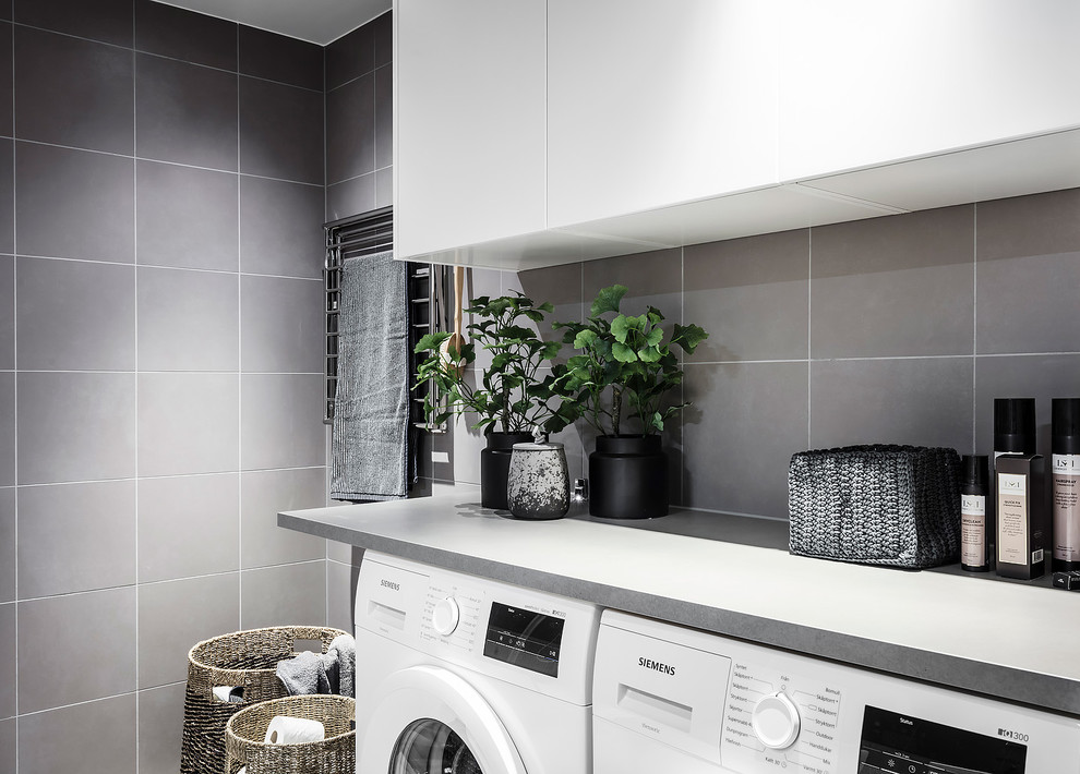 Photo of a large scandi utility room in Gothenburg with flat-panel cabinets, white cabinets, white walls, light hardwood flooring, a side by side washer and dryer and grey floors.