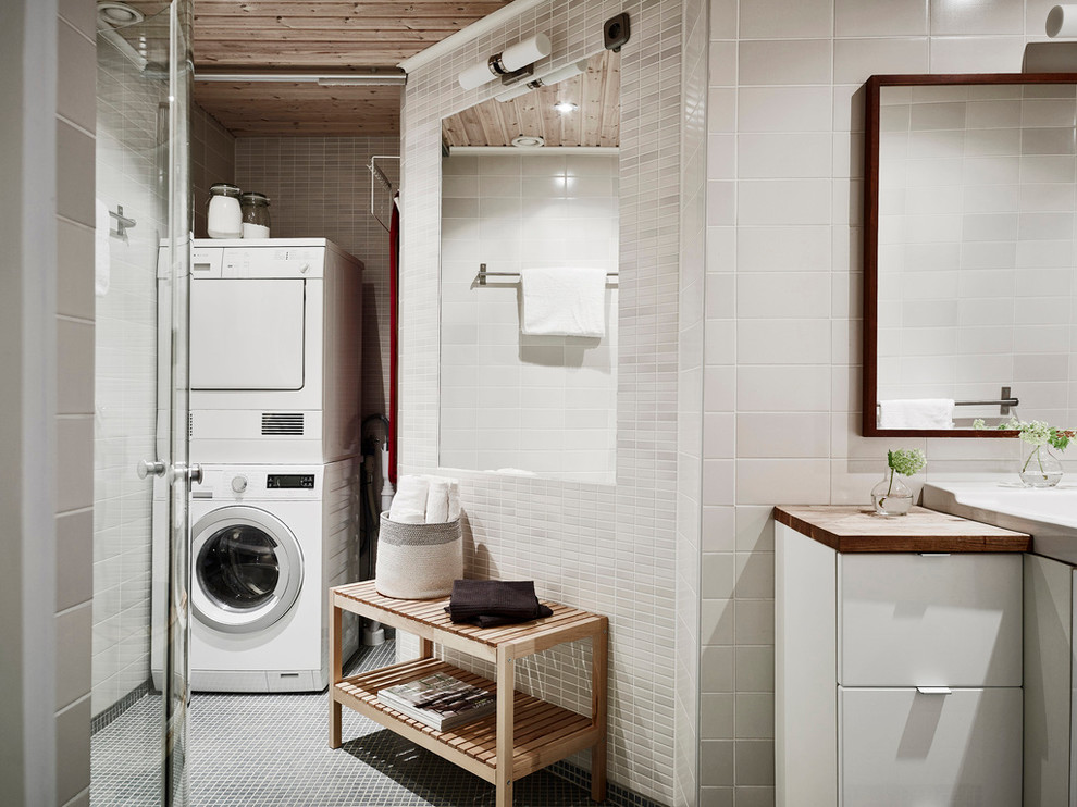 Exempel på en nordisk tvättstuga, med släta luckor, vita skåp, vita väggar, träbänkskiva och klinkergolv i porslin