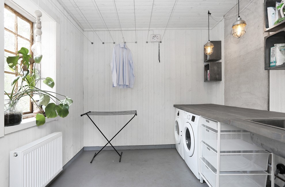 Diseño de cuarto de lavado lineal nórdico con fregadero de un seno, armarios abiertos, paredes blancas, lavadora y secadora juntas y suelo gris