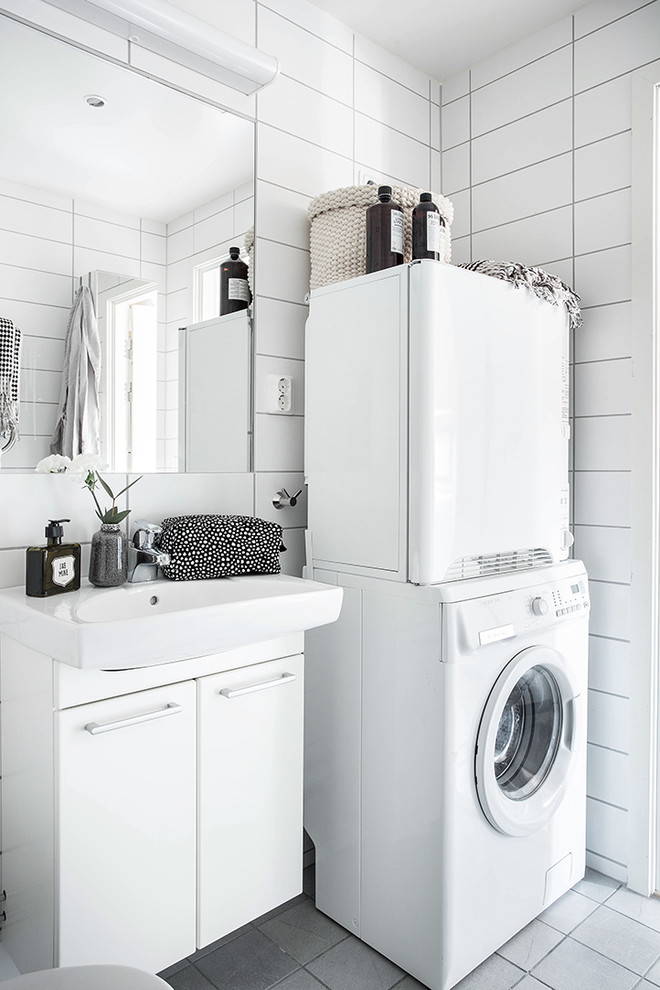 Diseño de lavadero multiusos escandinavo de tamaño medio con fregadero encastrado, armarios con paneles lisos, puertas de armario blancas, paredes blancas, suelo de baldosas de cerámica y lavadora y secadora apiladas