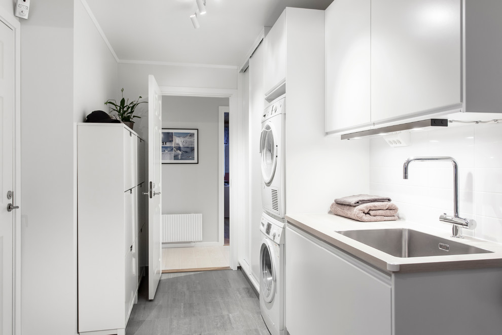 Foto di una lavanderia scandinava con lavello a vasca singola, ante lisce, ante bianche, pareti bianche, lavatrice e asciugatrice a colonna e pavimento grigio
