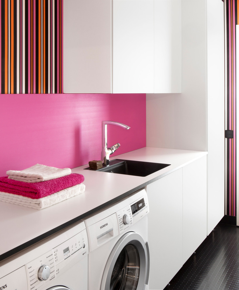 Inspiration för mellanstora moderna linjära tvättstugor enbart för tvätt, med en enkel diskho, släta luckor, vita skåp, rosa väggar, en tvättmaskin och torktumlare bredvid varandra, laminatbänkskiva och svart golv