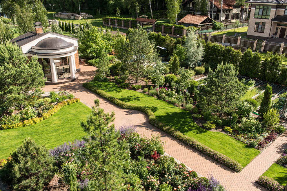 Exempel på en stor klassisk trädgård i full sol längs med huset på sommaren, med marksten i tegel och en trädgårdsgång