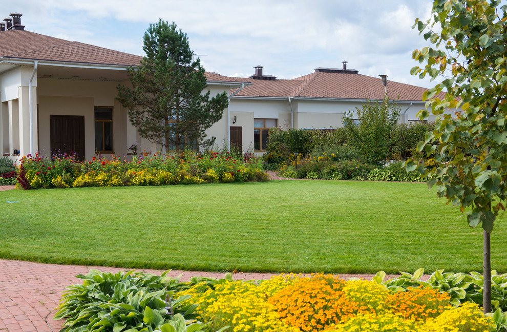 Immagine di un grande giardino esposto in pieno sole davanti casa in estate con pavimentazioni in mattoni