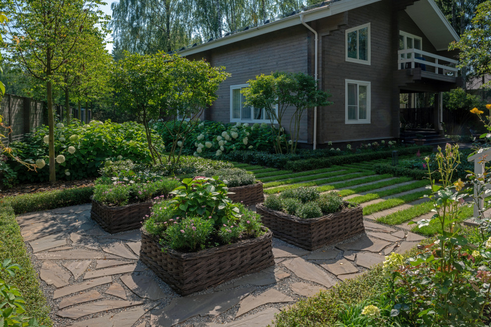 Modelo de jardín clásico de tamaño medio en verano en patio trasero con exposición parcial al sol, adoquines de piedra natural y macetero elevado