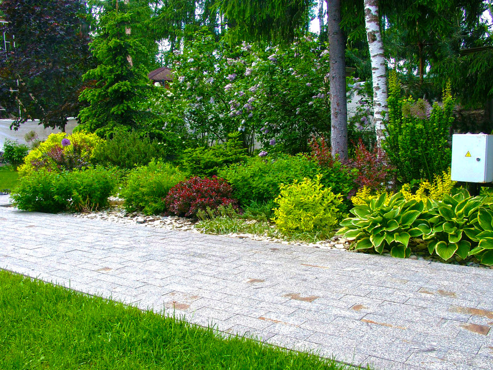 На фото: большой весенний засухоустойчивый сад на переднем дворе в современном стиле с клумбами, полуденной тенью и покрытием из каменной брусчатки с