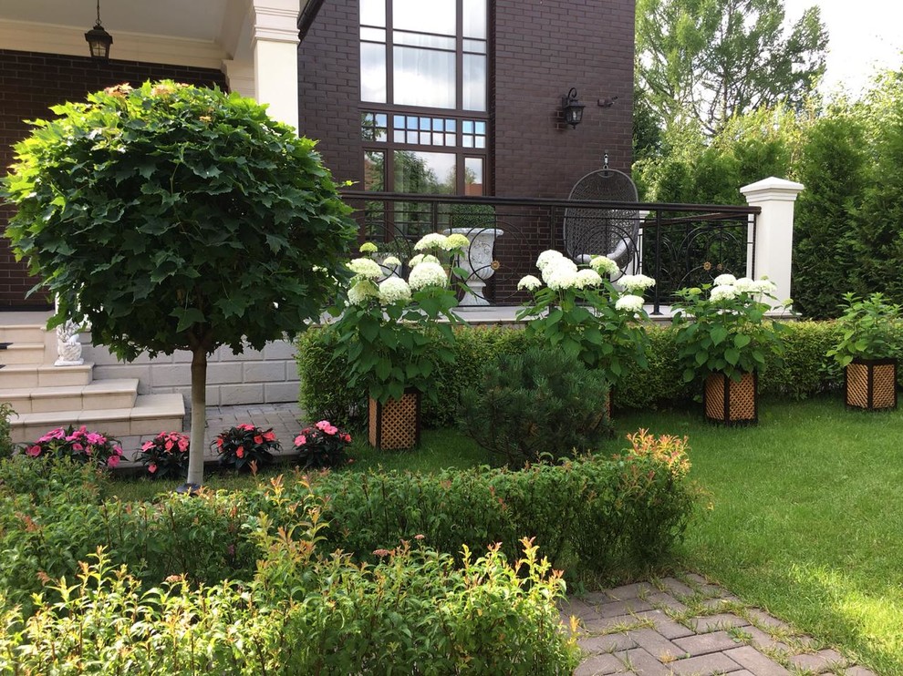 Diseño de jardín tradicional en verano en patio delantero con exposición parcial al sol y adoquines de ladrillo