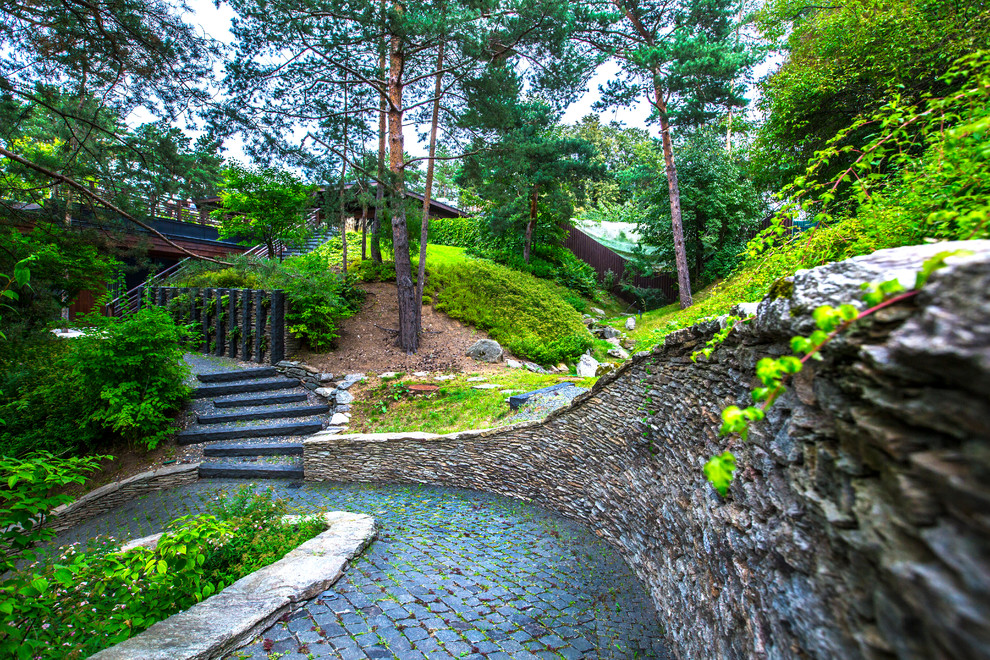 Exempel på en skandinavisk trädgård i delvis sol på sommaren, med en stödmur