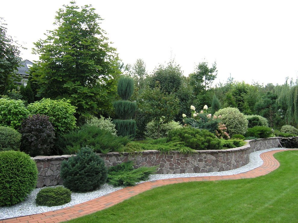 Exempel på en klassisk trädgård i full sol, med en stödmur och marksten i tegel