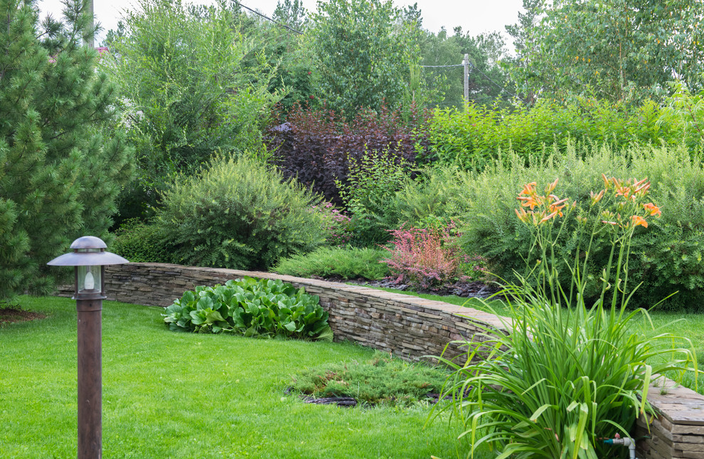 На фото: солнечный, летний участок и сад на переднем дворе с подпорной стенкой и хорошей освещенностью с