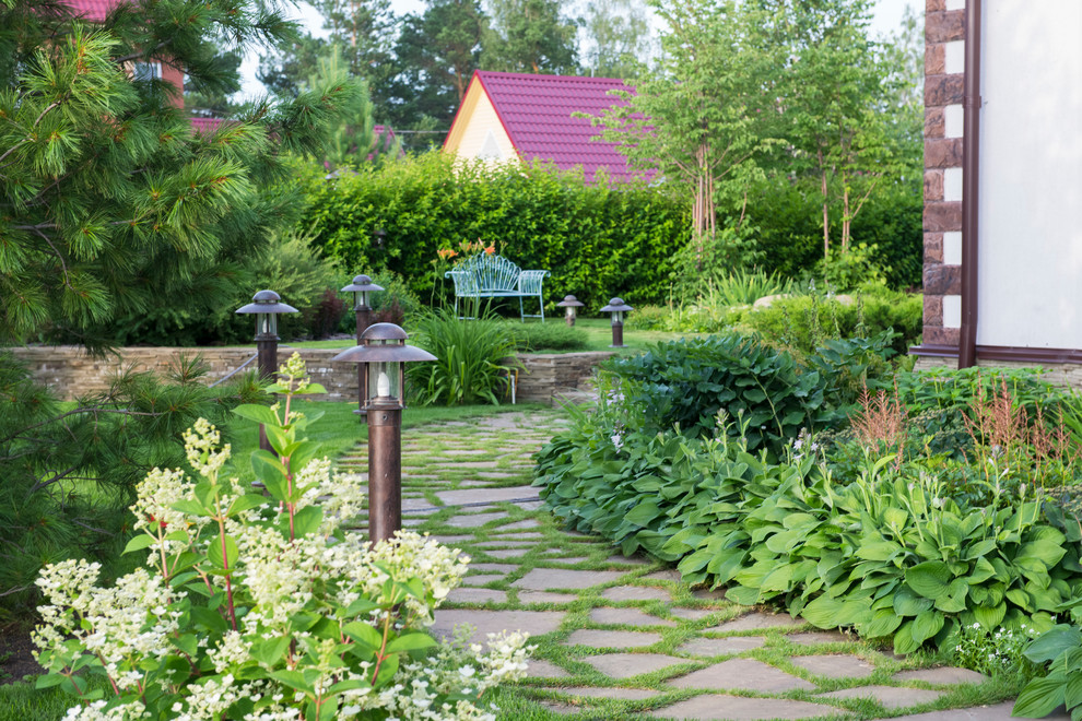Idéer för funkis trädgårdar i delvis sol framför huset på sommaren, med en stödmur och naturstensplattor