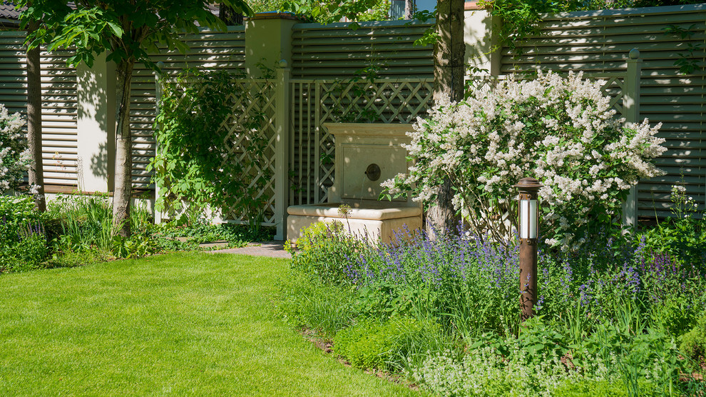 Modelo de jardín clásico de tamaño medio en verano en patio con exposición parcial al sol, fuente y jardín francés