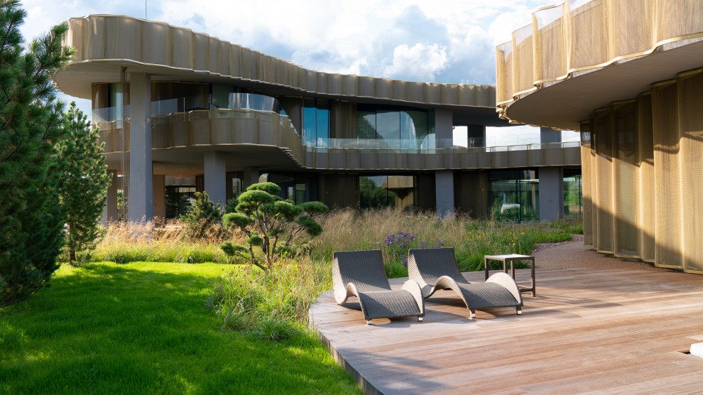 На фото: огромный солнечный, осенний участок и сад в стиле модернизм с перегородкой для приватности, хорошей освещенностью и настилом с