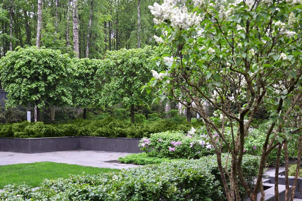 На фото: весенний регулярный сад на внутреннем дворе в современном стиле с полуденной тенью, покрытием из каменной брусчатки и подпорной стенкой с
