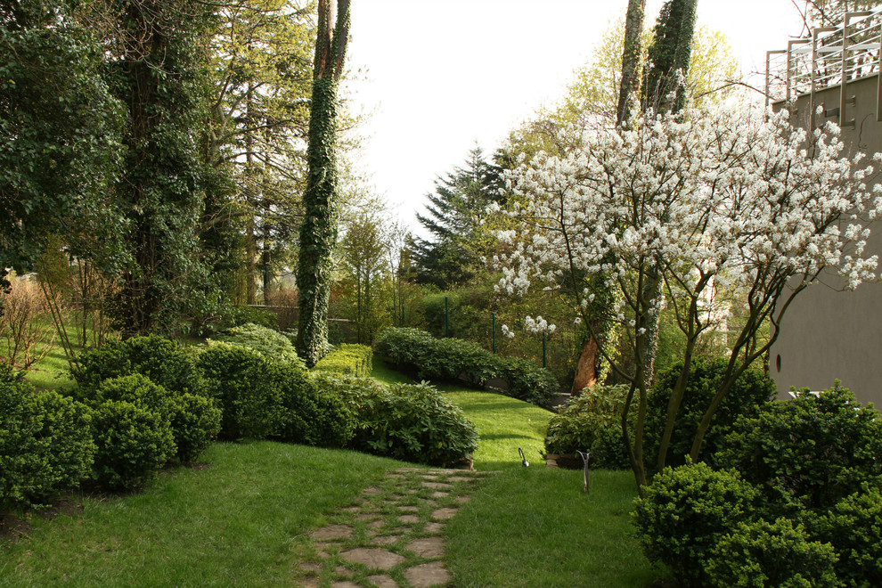 Inredning av en modern stor trädgård längs med huset på våren, med naturstensplattor