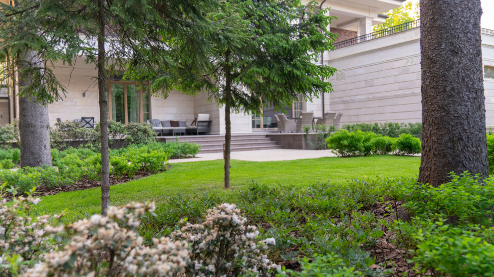 Aménagement d'un grand jardin sur cour au printemps avec une exposition partiellement ombragée et des pavés en béton.