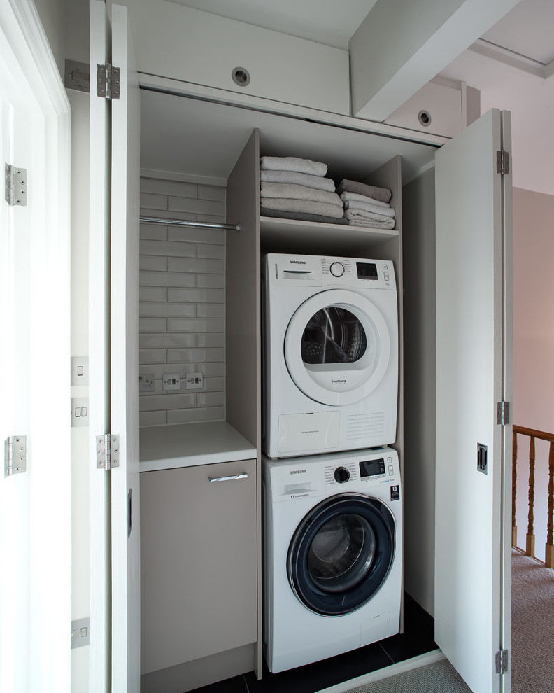 Einzeiliger, Kleiner Moderner Hauswirtschaftsraum mit Waschmaschinenschrank, flächenbündigen Schrankfronten, braunen Schränken, Waschmaschine und Trockner gestapelt, schwarzem Boden und weißer Arbeitsplatte in London