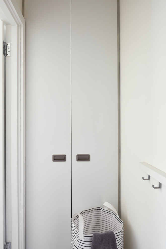 Imagen de armario lavadero lineal actual pequeño con armarios con paneles lisos, puertas de armario blancas, paredes blancas, suelo vinílico, lavadora y secadora integrada y suelo blanco