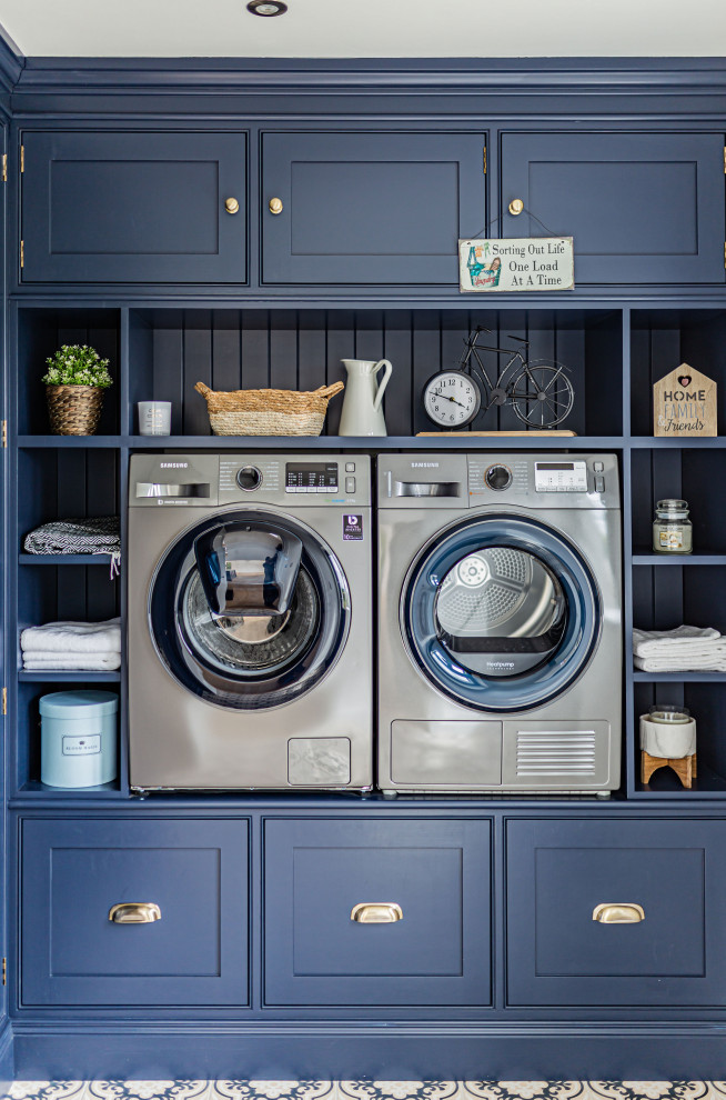 Foto på en vintage tvättstuga, med luckor med profilerade fronter, blå skåp, en tvättmaskin och torktumlare bredvid varandra och flerfärgat golv