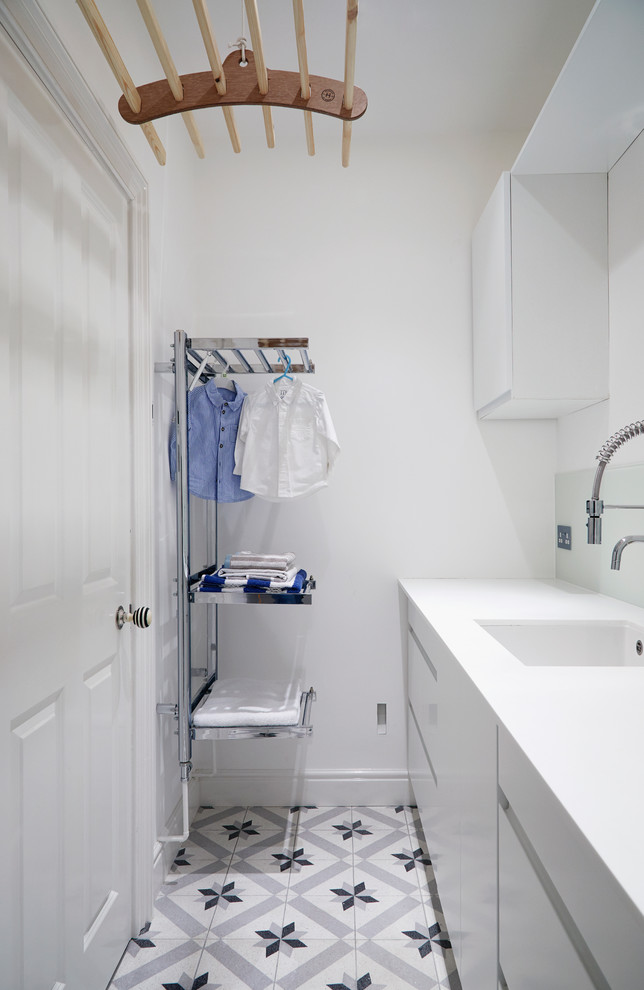 Foto på en mellanstor funkis parallell tvättstuga enbart för tvätt, med en nedsänkt diskho, släta luckor, vita skåp, bänkskiva i koppar, vita väggar, klinkergolv i keramik, en tvättpelare och grått golv