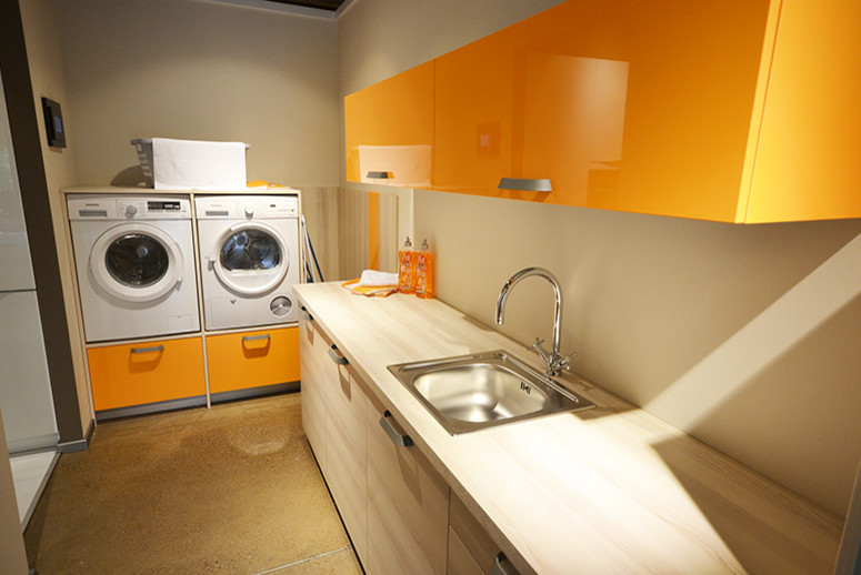 Immagine di una lavanderia minimal con ante lisce, ante arancioni, top in laminato e lavatrice e asciugatrice a colonna