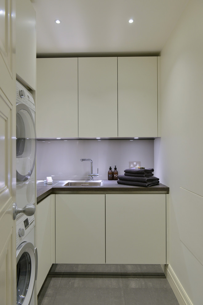 Foto på en liten funkis l-formad tvättstuga enbart för tvätt, med en integrerad diskho, släta luckor, vita skåp, laminatbänkskiva, vita väggar, klinkergolv i porslin och en tvättpelare