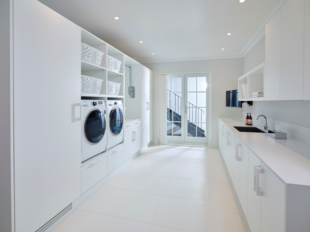 Multifunktionaler, Zweizeiliger Moderner Hauswirtschaftsraum mit Waschbecken, weißer Wandfarbe, Keramikboden, Waschmaschine und Trockner nebeneinander, flächenbündigen Schrankfronten, weißen Schränken und Mineralwerkstoff-Arbeitsplatte in London
