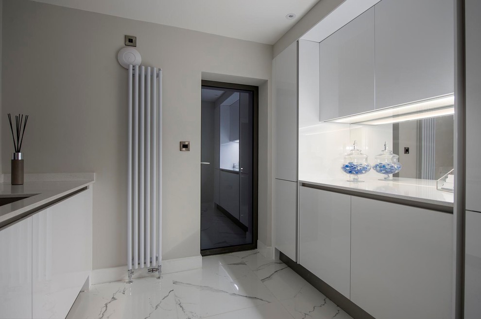 Small contemporary galley utility room in Other with a submerged sink, flat-panel cabinets, white cabinets, quartz worktops, beige walls, ceramic flooring, an integrated washer and dryer, white floors and white worktops.