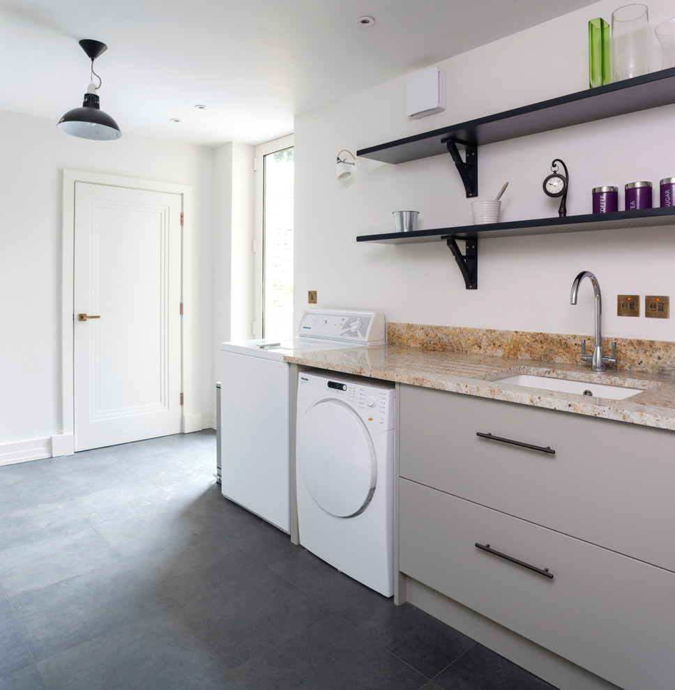 This is an example of a medium sized contemporary utility room in Wiltshire with a submerged sink, flat-panel cabinets, beige cabinets, white walls, a side by side washer and dryer, grey floors and granite worktops.