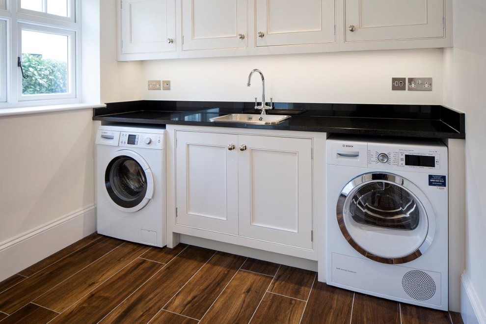 This is an example of a medium sized traditional single-wall utility room in Other with a built-in sink, beaded cabinets, white cabinets, granite worktops, beige walls, ceramic flooring, a side by side washer and dryer and brown floors.