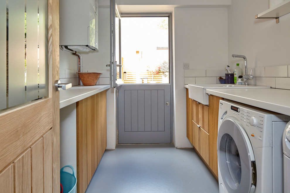 Small contemporary galley utility room in Berkshire with a belfast sink, flat-panel cabinets, medium wood cabinets, laminate countertops, vinyl flooring and a side by side washer and dryer.