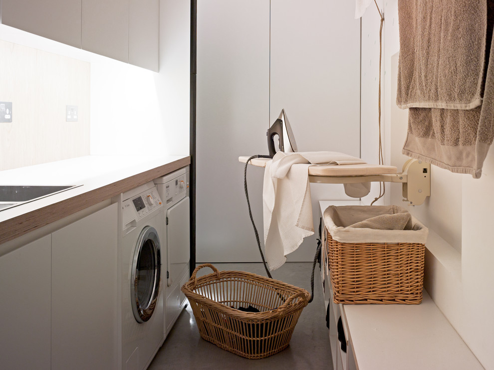 Imagen de lavadero contemporáneo con puertas de armario blancas, paredes blancas y suelo de cemento