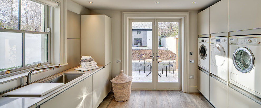 Inspiration for a large contemporary single-wall medium tone wood floor laundry room remodel in Dublin with a single-bowl sink, flat-panel cabinets, white cabinets, white walls and a side-by-side washer/dryer