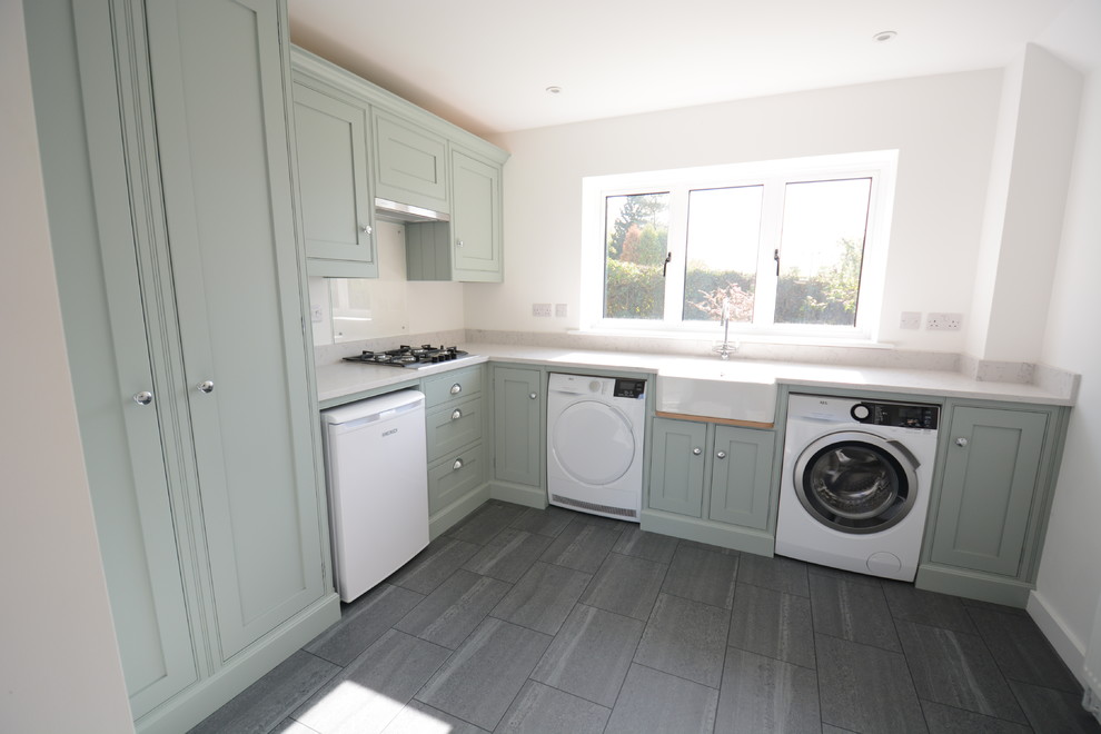 Small farmhouse l-shaped utility room in Sussex with a belfast sink, beaded cabinets, green cabinets, quartz worktops, white walls, porcelain flooring, black floors and white worktops.
