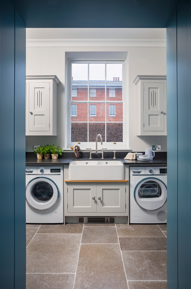 This is an example of a medium sized classic utility room in Hampshire with grey cabinets, granite worktops, black splashback, limestone flooring, shaker cabinets and a belfast sink.