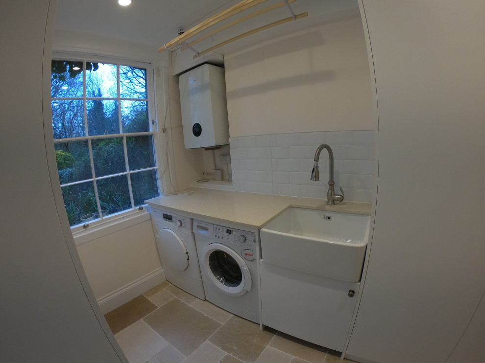 Foto på ett litet lantligt vit grovkök, med en undermonterad diskho, vita väggar och tvättmaskin och torktumlare byggt in i ett skåp