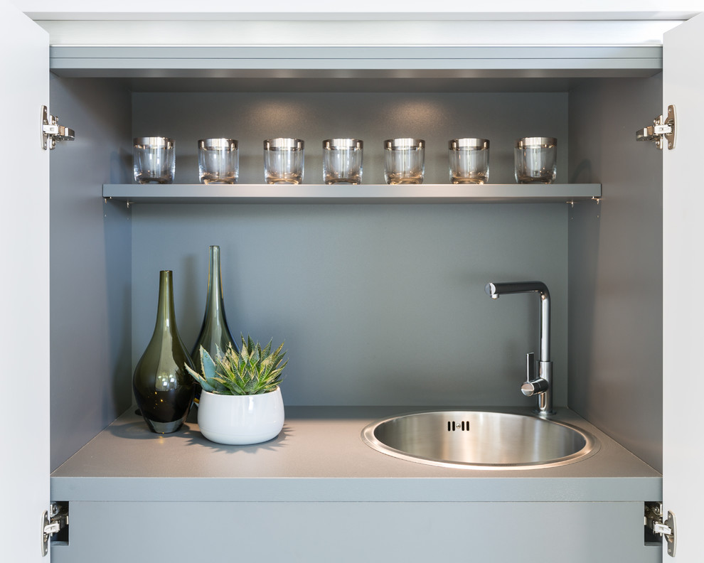 Foto på en liten funkis grå linjär liten tvättstuga, med en enkel diskho, släta luckor, grå skåp, laminatbänkskiva, beige väggar, heltäckningsmatta och grått golv